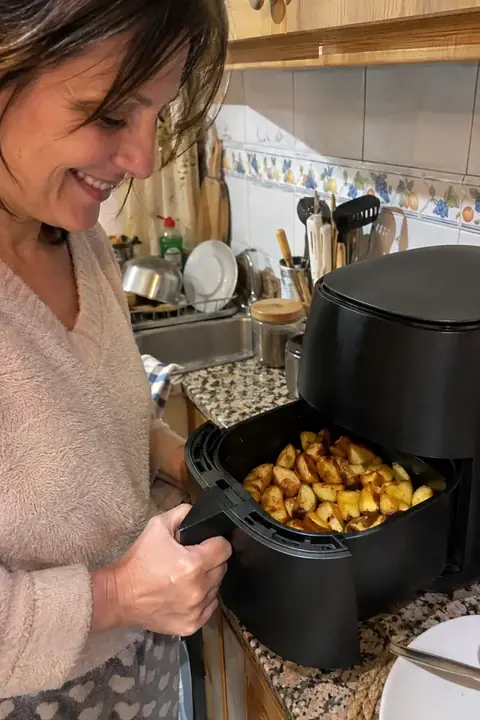 Mujer sacando de la freidora de aire la cesta con patatas doradas