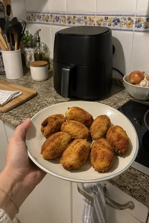 Mano sosteniendo un plato de croquetas caseras en una cocina con azulejos